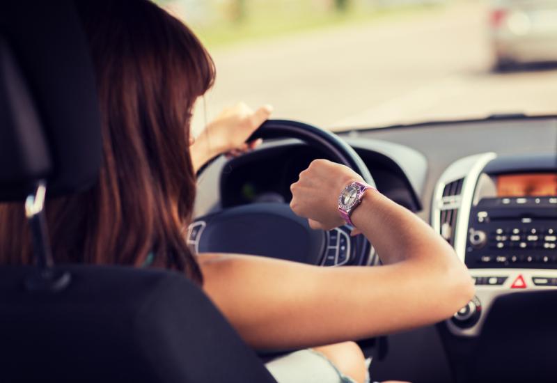 Frau sieht beim Autofahren auf die Uhr